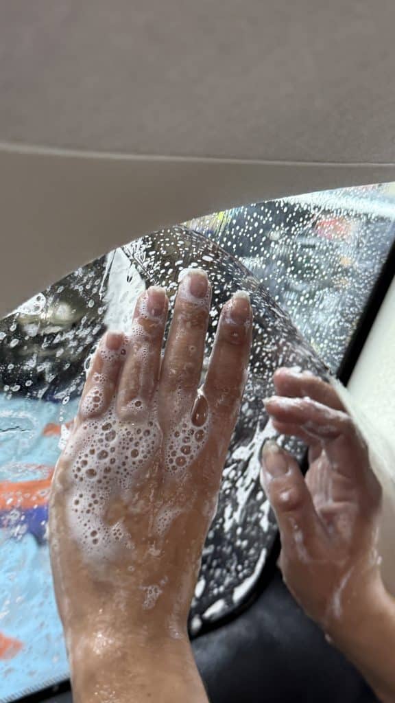 Mains mouillées appliquant un film teinté sur une vitre de voiture