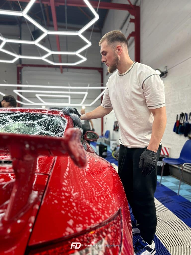 Homme lavant voiture rouge dans garage lumineux