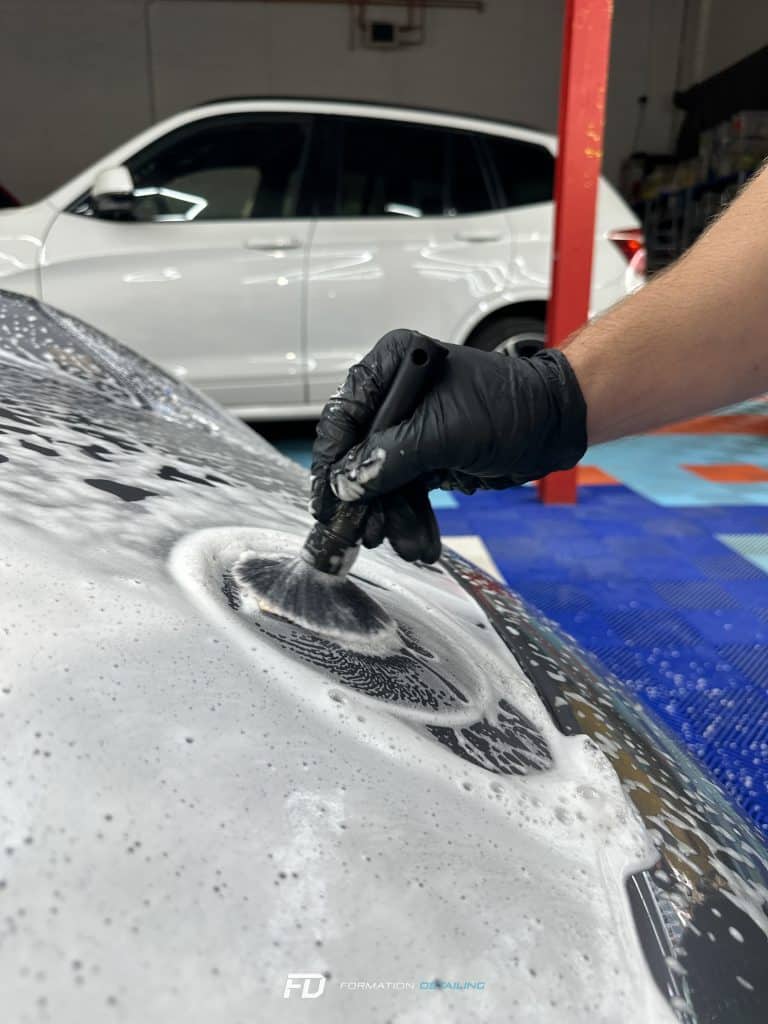 Main gantée polissant capot de voiture blanche