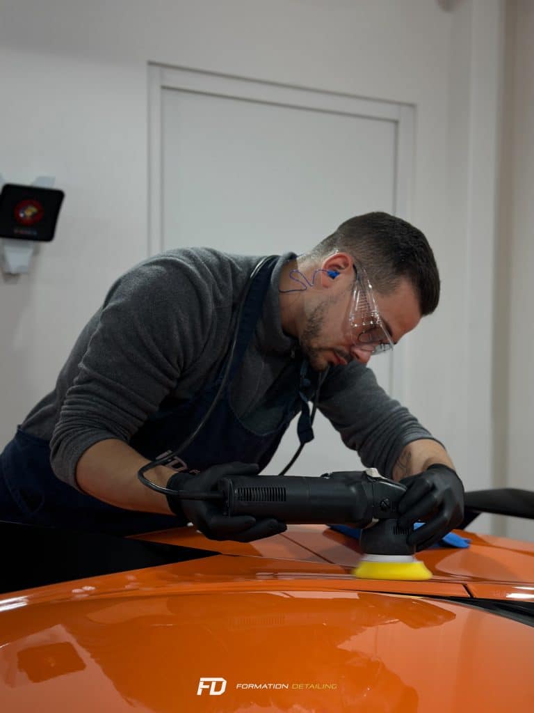 Homme polissant voiture orange en atelier